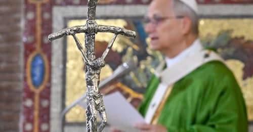 Silver sculpture of Christ on cross with priest in background